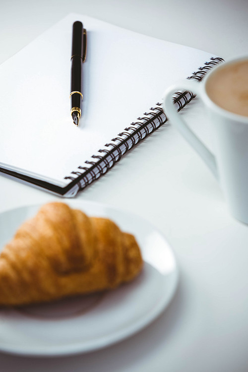 Notebook with pen and coffee by food on table