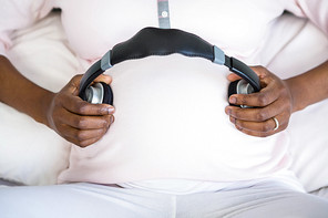 Pregnant woman holding headphone on belly on bed