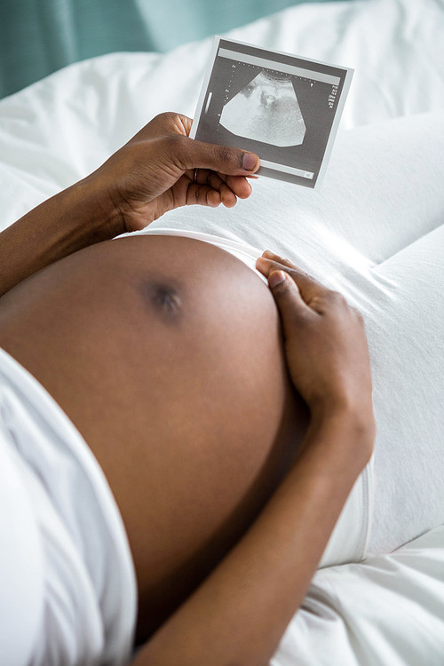 Pregnant woman looking at ultrasound pictures lying on her bed