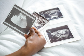 Feminine hands holding ultrasound pictures in the bedroom