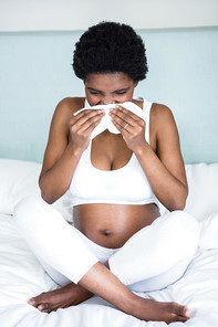 Pregnant woman blowing her nose at home