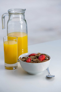 View of bowl of cereals and orange juice on white table