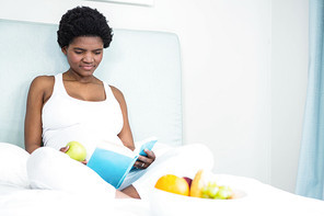 Pregnant woman reading a book lying on her bed