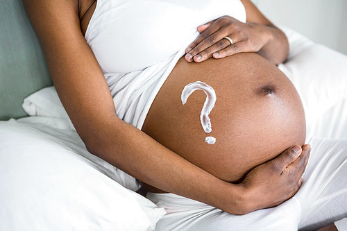 Pregnant woman applying cream on her belly at home