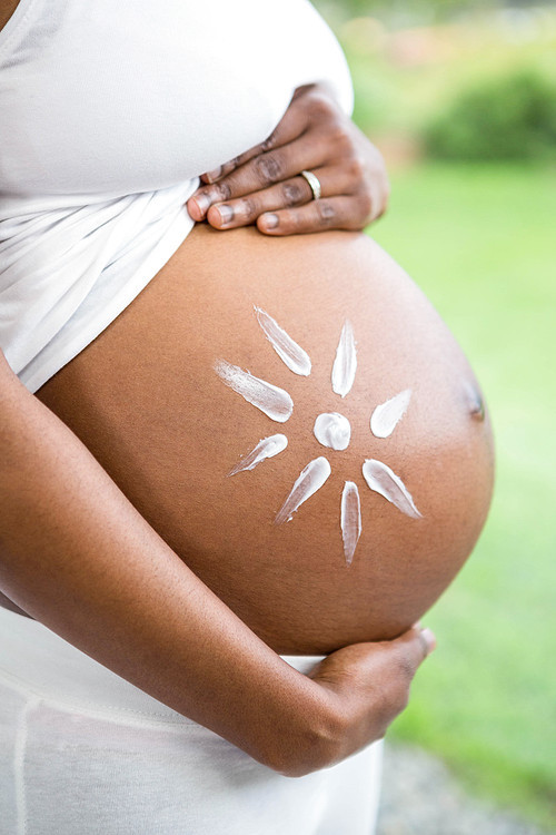 Pregnant woman applying cream on her belly at home