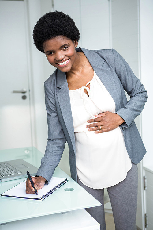 Pregnant businesswoman writing on notebook in office