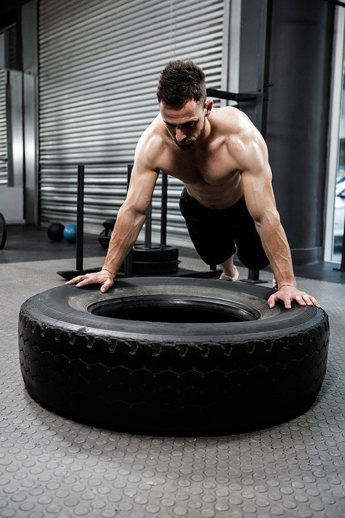 Shirtless man flipping heavy tire at the crossfit gym