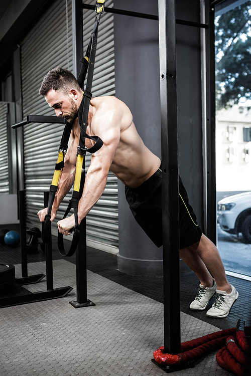 Shirtless man hanging at the rope at the crossfit gym