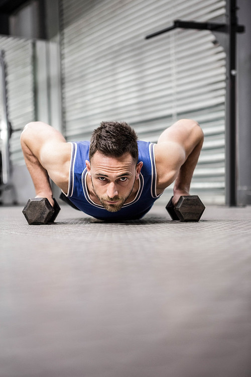 Muscular man doing push up wioth dumbbells at the crossfit gym