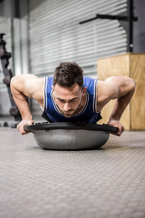 Muscular man doing push up on bosu ball at the crossfit gym