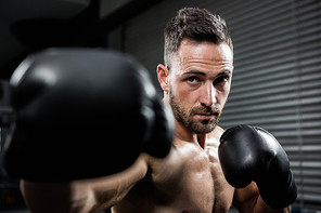 Determined shirtless man with boxe gloves hitting at crossfit gym