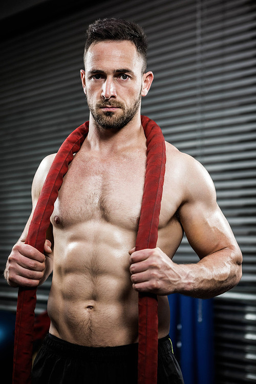 Shirtless man with battle rope around neck at the crossfit gym