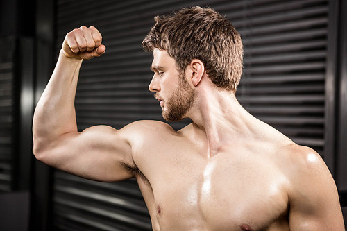 Shirtless man flexing biceps at the crossfit gym