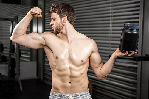 Shirtless man showing biceps and holding can at the crossfit gym