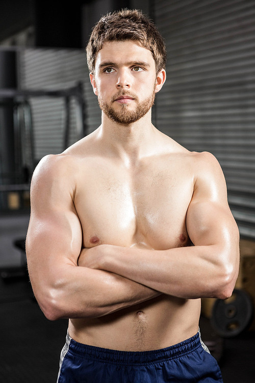 Determined shirtless man with arms crossed at the crossfit gym