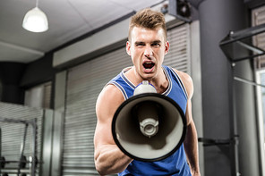 Muscular trainer shouting on megaphone at the crossfit gym