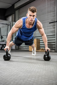 Muscular man doing push up with kettlebells at the crossfit gym