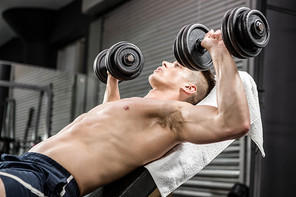 Shirtless man lifting heavy dumbbells on bench at the crossfit gym