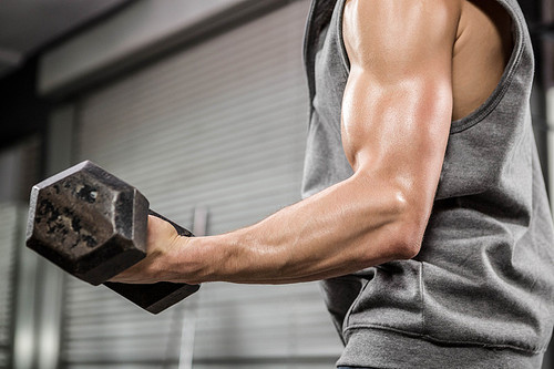 Muscular man with grey jumper lifting dumbbell at the crossfit gym