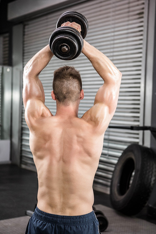 Shirtless man lifting heavy dumbbell at the crossfit gym