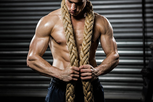 Shirtless man with battle rope around neck at the crossfit gym