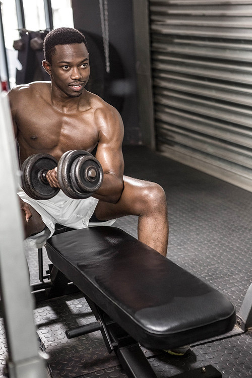 Shirtless man lifting dumbbell on bench at the crossfit gym