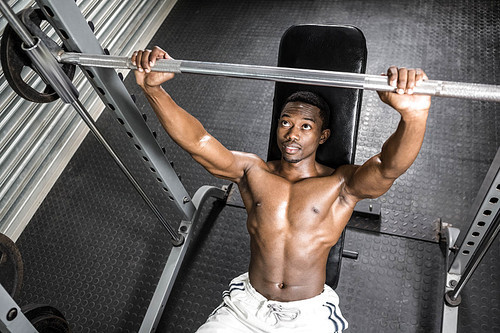 Shirtless man lifting barbell on bench at the crossfit gym