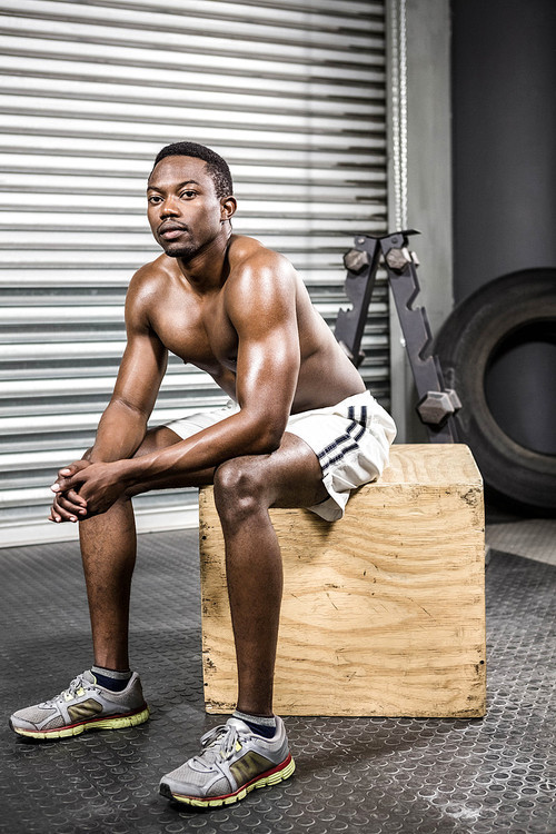 Shirtless man sitting on wooden block at the crossfit gym