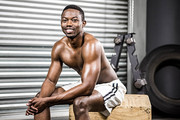 Smiling shirtless man sitting on wooden block at the crossfit gym