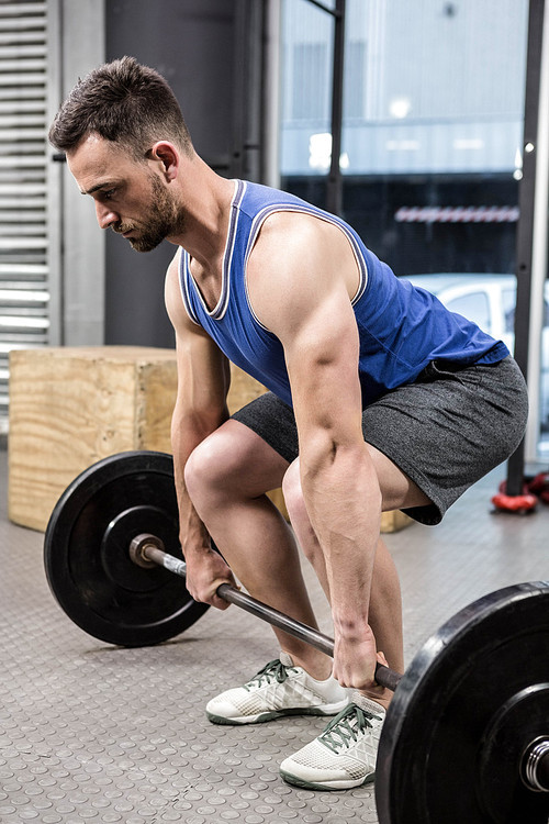 Muscular man lifting barbell at the crossfit gym