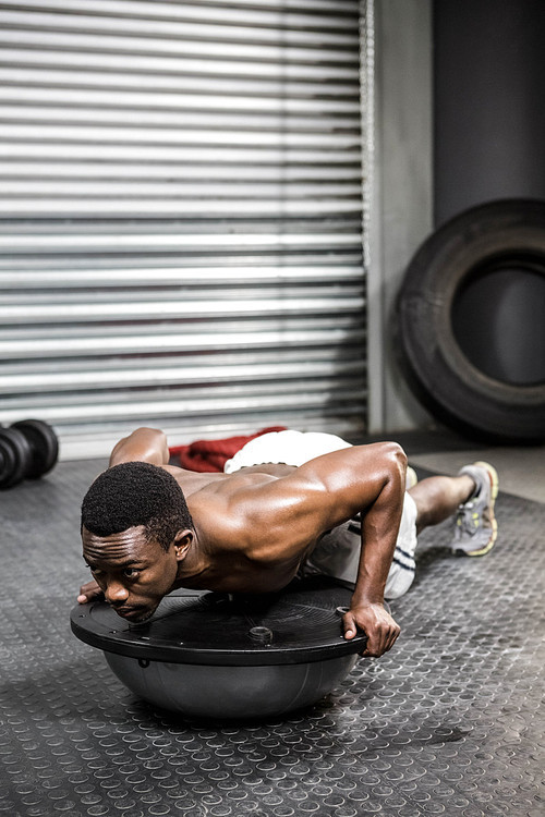 Muscular man doing push up on bosu ball at the crossfit gym