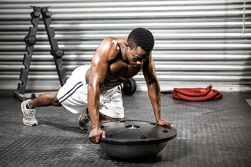 Muscular man doing push up on bosu ball at the crossfit gym