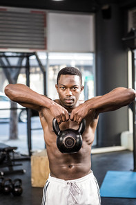 Shirtless man lifting heavy kettlebell at the crossfit gym