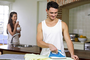 Man ironing a shirt while woman having breakfast in background