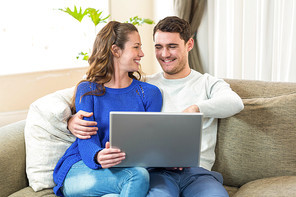 Young couple sitting on sofa and using laptop in living room