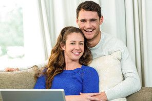 Young couple sitting on sofa and using laptop in living room