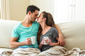 Young couple cuddling on sofa while having coffee in living room