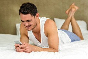 Young man texting and smiling while lying on bed with his phone