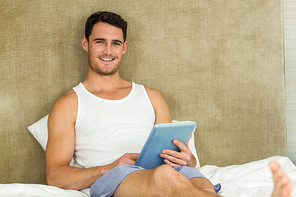 Portrait of young man smiling while using a digital tablet in bedroom