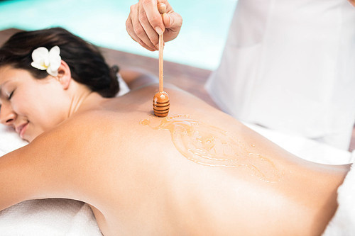 Woman receiving a honey massage from masseur near pool