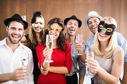 Friends with masks on holding champagne glasses laughing at camera