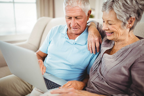 Senior couple sitting on sofa and looking at laptop in living room