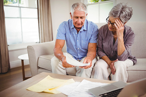 Senior man sitting with woman on sofa and showing documents in living room