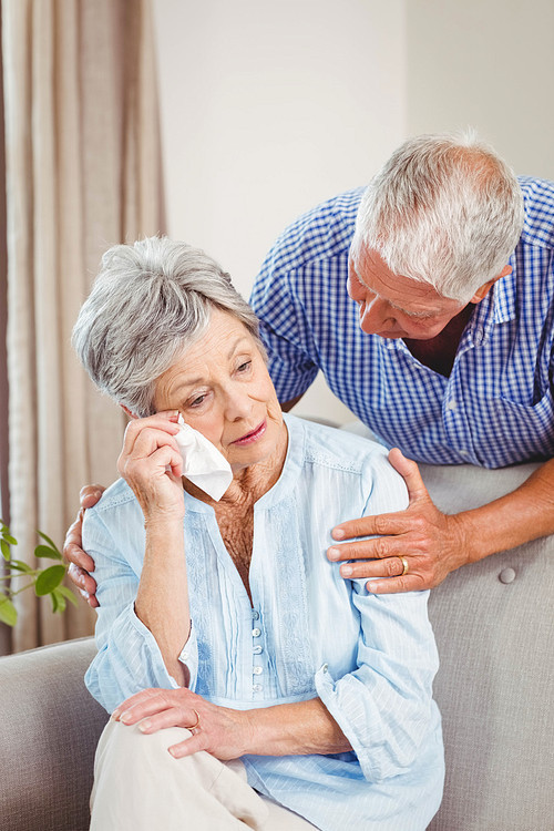 Senior man talking to upset senior woman in living room