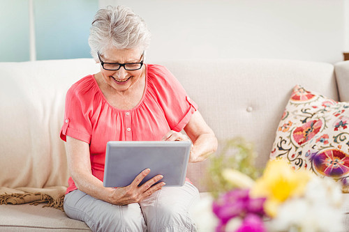Senior woman smiling while using digital tablet at home