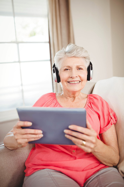 Portrait of happy senior woman listening to music on digital tablet