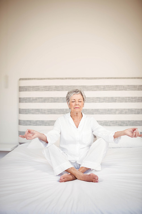 Senior woman meditating on bed in bedroom