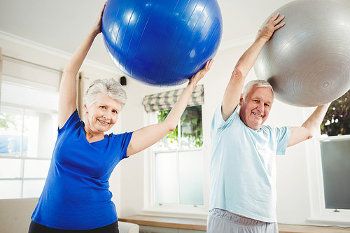 Senior couple lifting exercise ball while exercising