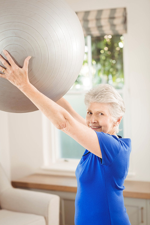 Portrait of senior woman lifting exercise ball while exercising at home