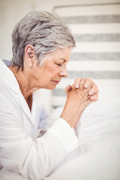 Worried senior woman sitting on bed in bedroom